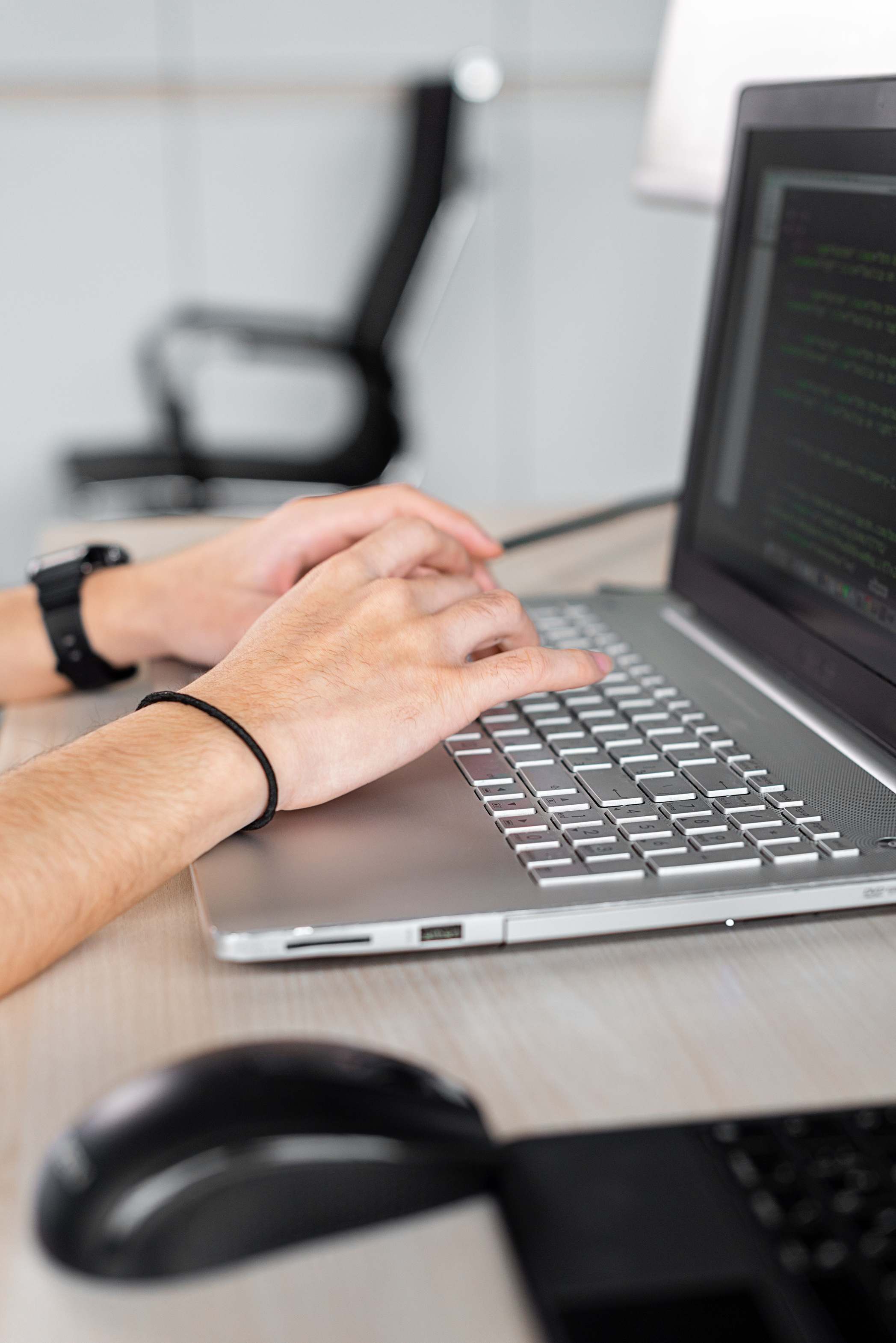 Hands typing on a keyboard at a laptop, person typing in a modern office