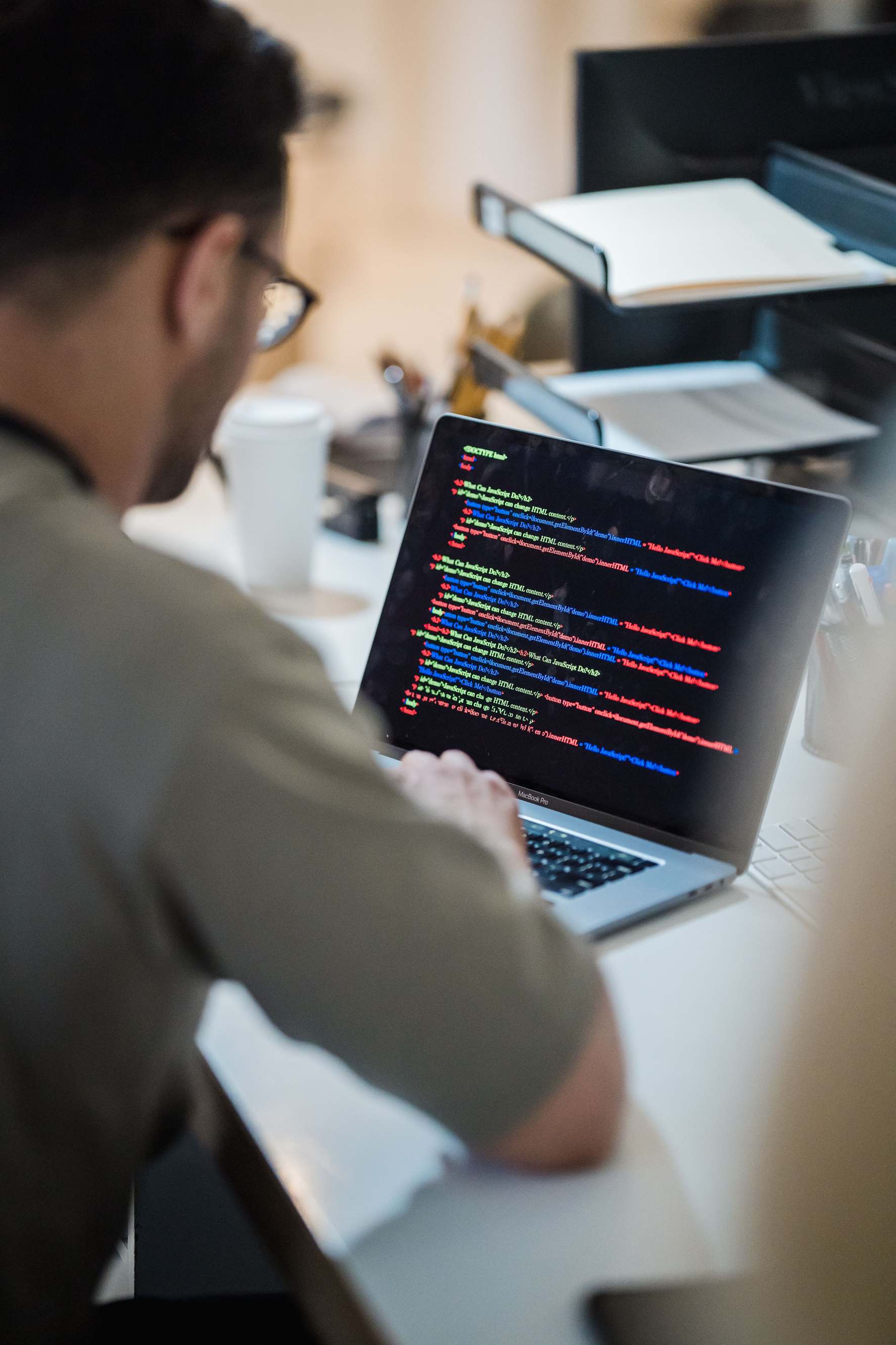 Office workspace with computer monitors, programmer coding on a laptop in an office environment